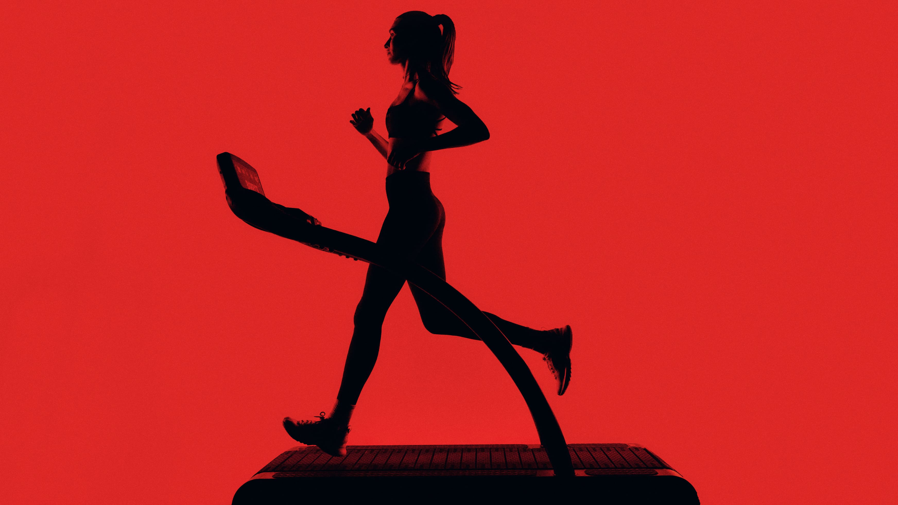A runner in silhouette, mid-stride on a treadmill, lit in red inside the Barry's Red Room.
